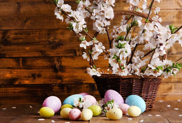 Összetétele a virágzó ágak és a húsvéti tojás, fonott kosár, fából készült háttér — Stock Fotó