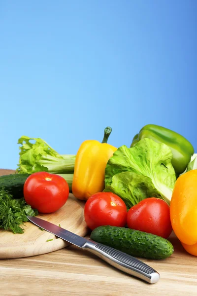 Samenstelling met gehakte kruiden op snijplank en verse groenten, op houten tafel, op blauwe achtergrond — Stockfoto