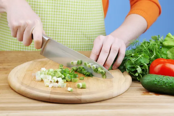 Female hands chopping onion on wooden board, close-up, on blue background — Stock Photo, Image