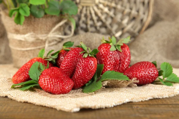 Fragole con foglie su tovagliolo di sacco, su sfondo di legno — Foto Stock