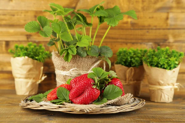 Strawberries with leaves on wicker mat, on wooden background — Stock Photo, Image