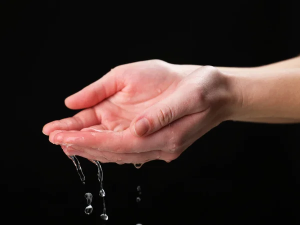 Emberi kezek őket a fekete háttér előtt fröcskölő víz — Stock Fotó
