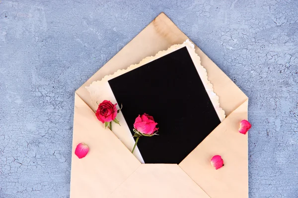 Envelope velho com papel fotográfico em branco e belas rosas rosa secas em fundo de madeira — Fotografia de Stock