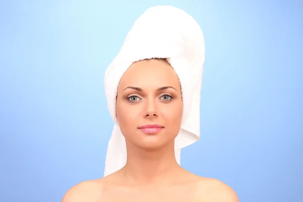 Beautiful young woman after shower with a towel on her head on blue background close-up — Stockfoto