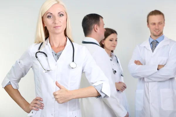 Dokter staan voor collega's op grijze achtergrond — Stockfoto