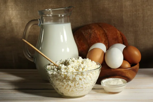 Tasty dairy products on wooden table, on sacking background — Stock Photo, Image