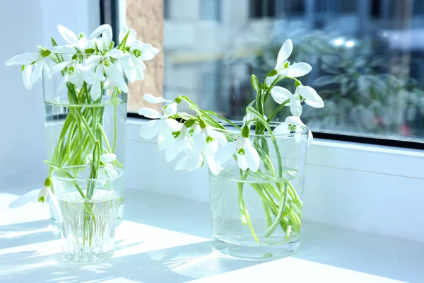 Beautiful bouquets of snowdrops in vases on windowsill — Stock Photo, Image