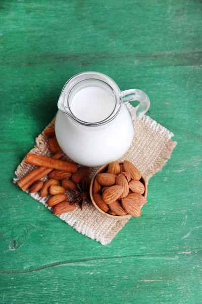 Almond milk in jug with almonds in bowl, on color wooden background — Stock Photo, Image