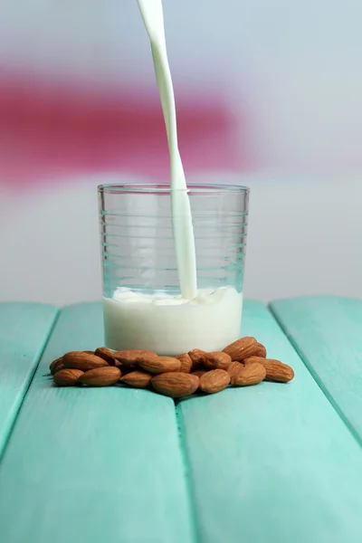 O leite de amêndoa é derramado em vidro, na tabela de madeira da cor, no fundo claro — Fotografia de Stock