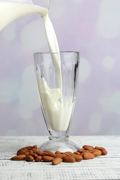 Mandelmilch wird in Glas gegossen, auf farbigem Holztisch, auf hellem Hintergrund — Stockfoto