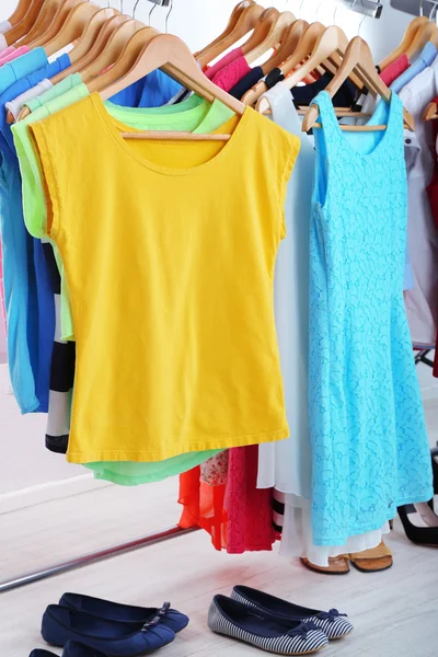 Verschiedene Kleidungsstücke auf Kleiderbügeln und Schuhe auf hellem Hintergrund — Stockfoto