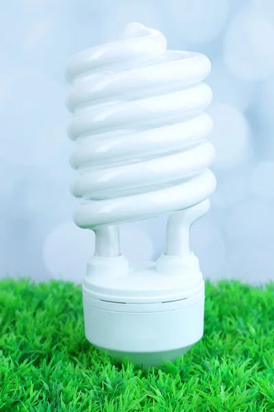 Energiesparlampe auf grünem Gras, auf hellem Hintergrund — Stockfoto