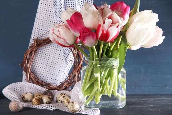 Komposition mit Ostereiern und schönen Tulpen im Glaskrug auf farbigem Holzhintergrund — Stockfoto