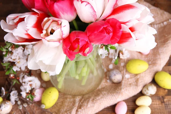 Composition avec des œufs de Pâques et de belles tulipes dans une cruche en verre sur fond en bois — Photo
