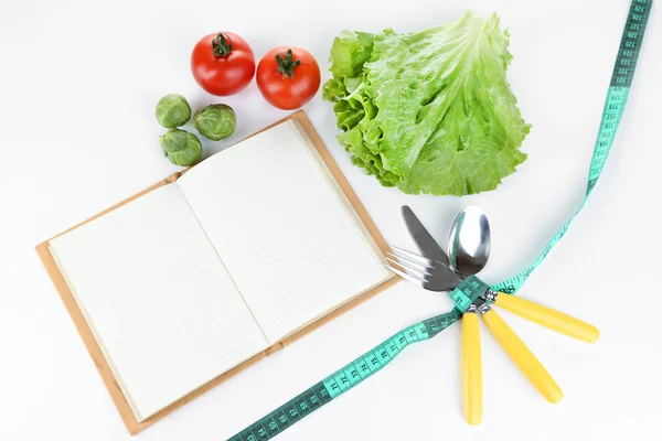 Besteck mit Maßband gebunden und Buch mit Gemüse isoliert auf weiß — Stockfoto