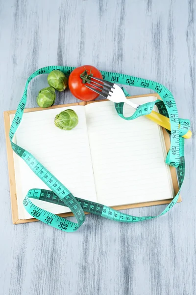 Livre avec ruban à mesurer et légumes sur fond en bois — Photo