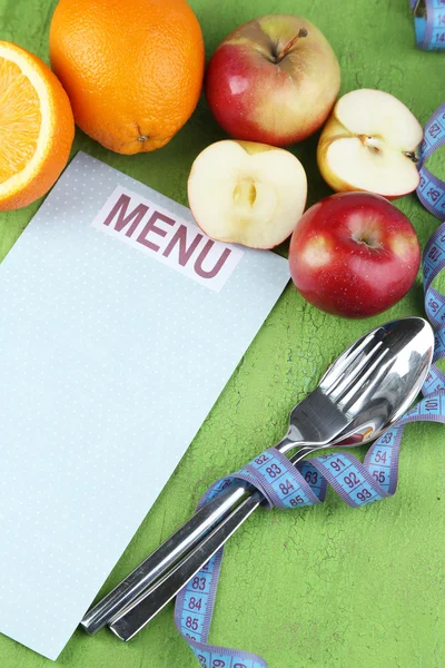 Cutlery tied with measuring tape and menu with fruits on wooden background — Stock Photo, Image