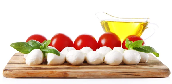 Composition with tasty mozzarella cheese balls, basil and red tomatoes, olive oil on cutting board, isolated on white