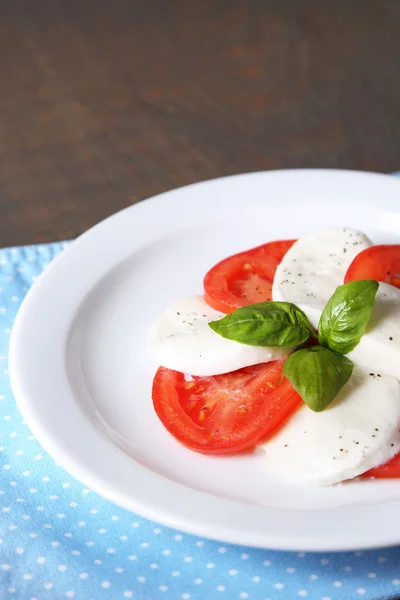 Caprese-Salat mit Mozarella, Tomaten und Basilikum auf Teller, auf Holztischhintergrund — Stockfoto