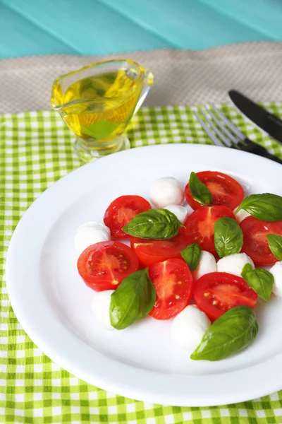 Caprese salade met mozarella kaas, tomaten en basilicum op plaat, op houten tafel achtergrond — Stockfoto