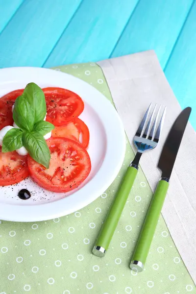 Caprese-Salat mit Mozarella, Tomaten und Basilikum auf Teller, auf Holztischhintergrund — Stockfoto