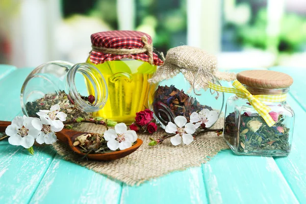 Assortment of herbs and tea and honey in glass jars on wooden table, on bright background — Stock Photo, Image