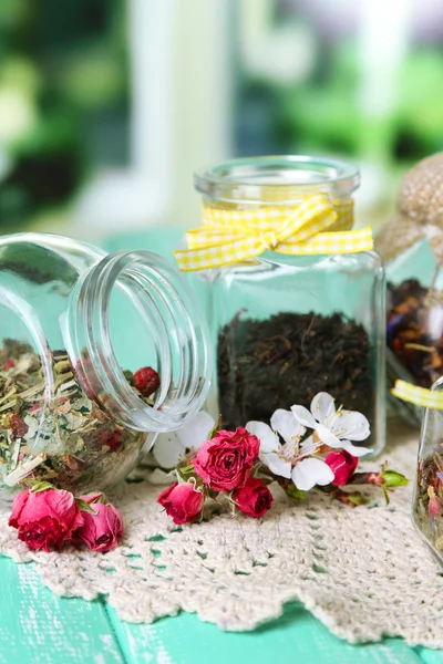 Assortment of herbs and tea in glass jars on wooden table, on bright background — Stock Photo, Image