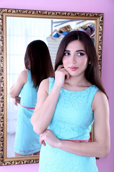 Όμορφο κορίτσι που προσπαθεί το φόρεμα κοντά καθρέφτη σε δωμάτιο — Φωτογραφία Αρχείου