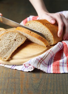 Ahşap tahtada ekmek kesen kadın elleri, yakın plan.