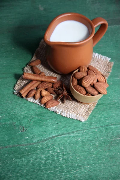 Миндальное молоко в кувшине с миндалем в миске, на цветном деревянном фоне — стоковое фото