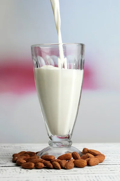 Il latte di mandorla viene versato nel vetro, sul tavolo di legno a colori, su sfondo chiaro — Foto Stock