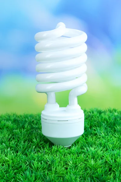 Energy saving light bulb on green grass, on bright background — Stock Photo, Image