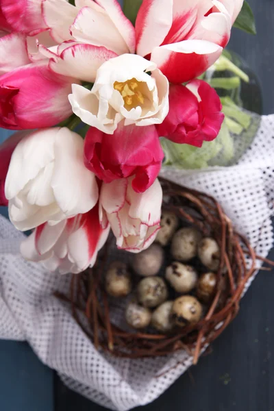复活节彩蛋与美丽的郁金香，在玻璃水罐上彩色木背景组成 — 图库照片
