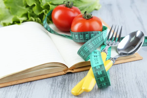 Cutlery tied with measuring tape and book with vegetables on wooden background — Stock Photo, Image