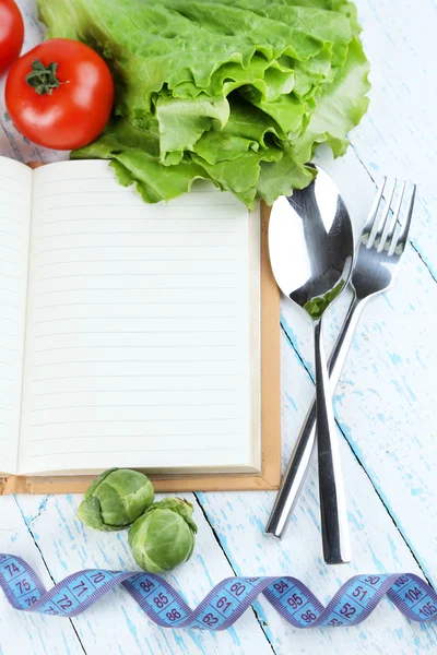 Libro con cubiertos, cinta métrica y verduras sobre fondo de madera — Foto de Stock