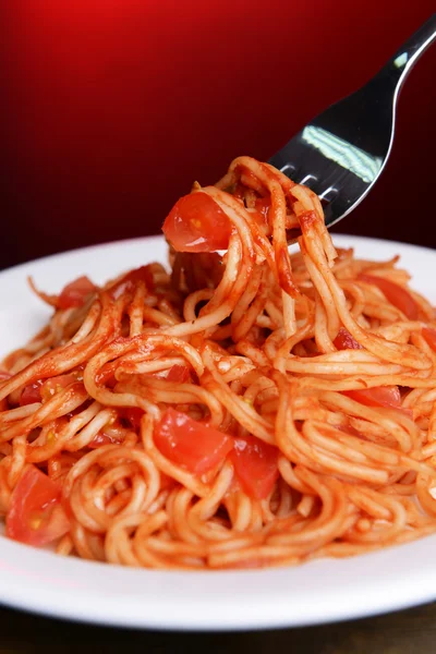 Pasta with tomato sauce on plate on table on red background — Stock Photo, Image