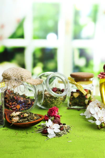 Assortiment van kruiden en thee in glazen potten op houten tafel, op lichte achtergrond — Stockfoto