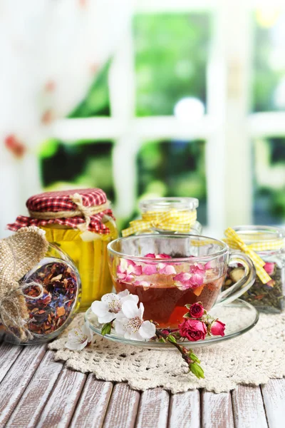 Auswahl an Kräutern, Tee und Honig in Glasgläsern und Tasse Heißgetränk auf Holztisch, auf hellem Hintergrund — Stockfoto