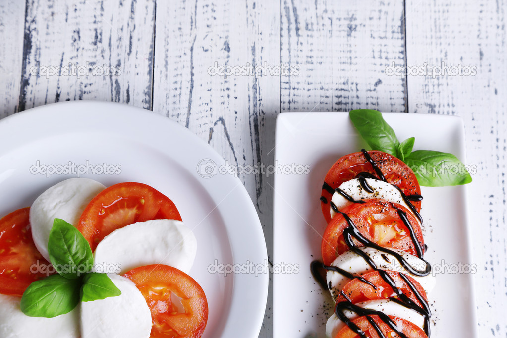 Caprese salad with mozarella cheese, tomatoes and basil on plates, on wooden table background