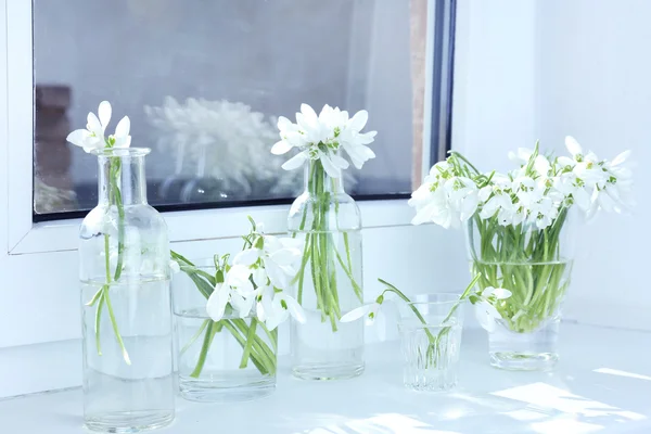 Beautiful bouquets of snowdrops in vases on windowsill — Stock Photo, Image