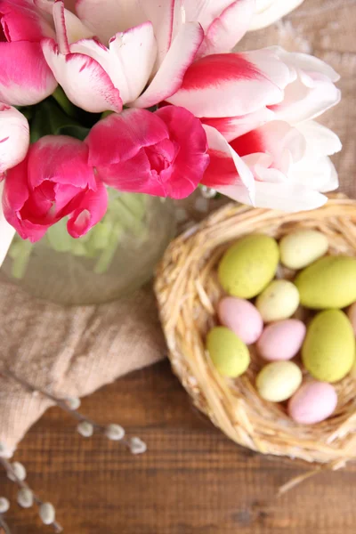 Composition with Easter eggs and beautiful tulips in glass jug on wooden background — Stock Photo, Image