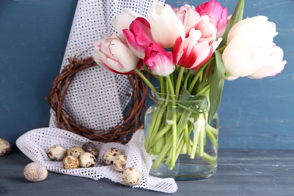 Композиція з великодніми яйцями і красивими тюльпанами в скляному глечику на кольоровому дерев'яному фоні — стокове фото