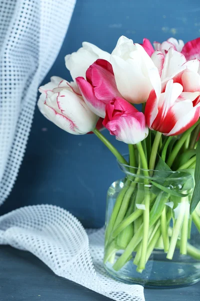 Krásné tulipány ve skleněné konvici na barevné dřevěné pozadí — Stock fotografie
