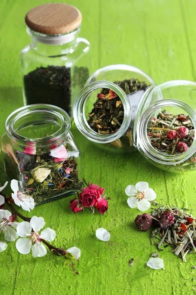 Auswahl an Kräutern und Tee in Glasgefäßen auf Holzgrund — Stockfoto