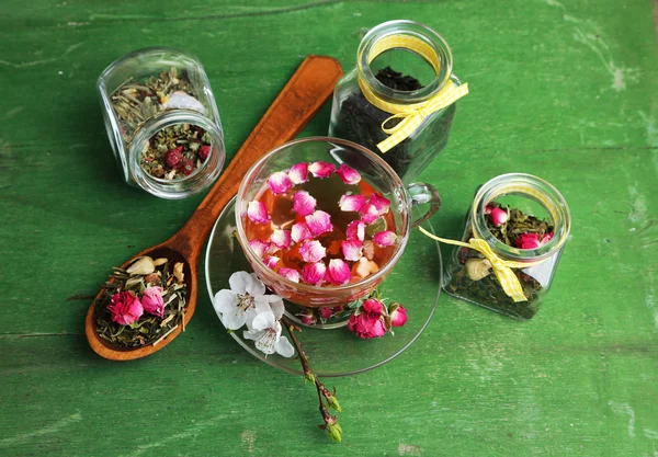 Asortyment zioła, herbaty w słoikach i filiżankę gorącego napoju na drewniane tła — Zdjęcie stockowe