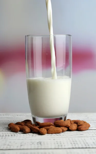 Mandula-tejet öntenek, üveg, színes fából készült asztal, a világos háttér — Stock Fotó