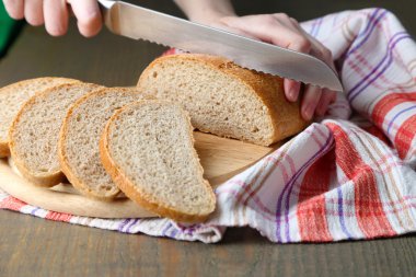 Ahşap tahtada ekmek kesen kadın elleri, yakın plan.