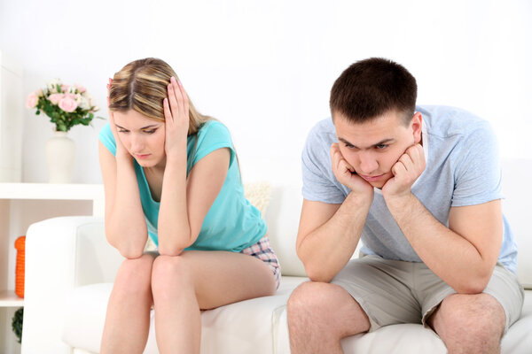 Portrait of young man and woman  conflict sitting on sofa argue unhappy, on home interior background