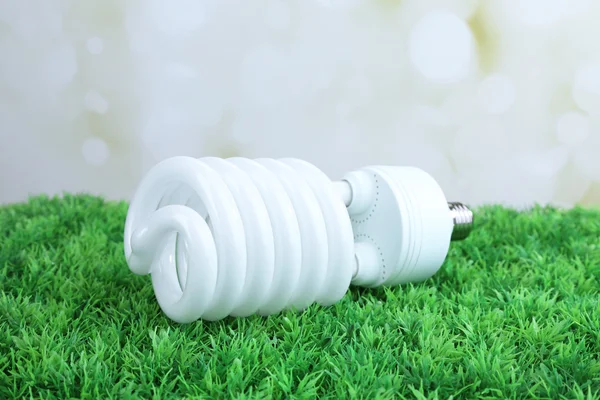 Lâmpada de poupança de energia na grama verde, no fundo claro — Fotografia de Stock