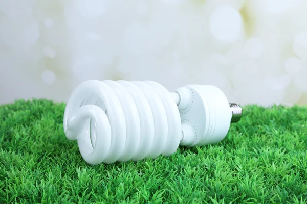 Energiesparlampe auf grünem Gras, auf hellem Hintergrund — Stockfoto